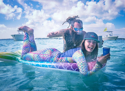 A woman floating on a mermaid pool float in the ocean and she is wearing mermaid leggings